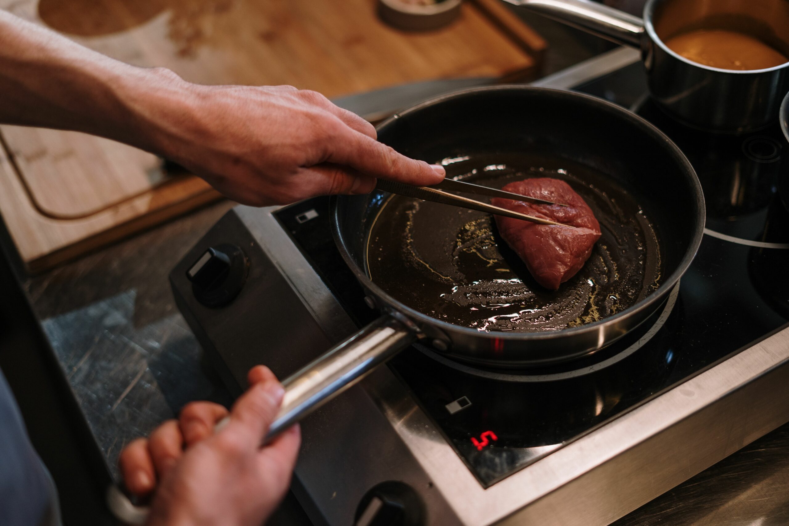 Cocinero sujetando con pinzas un filete que se cocina en una sartén caliente