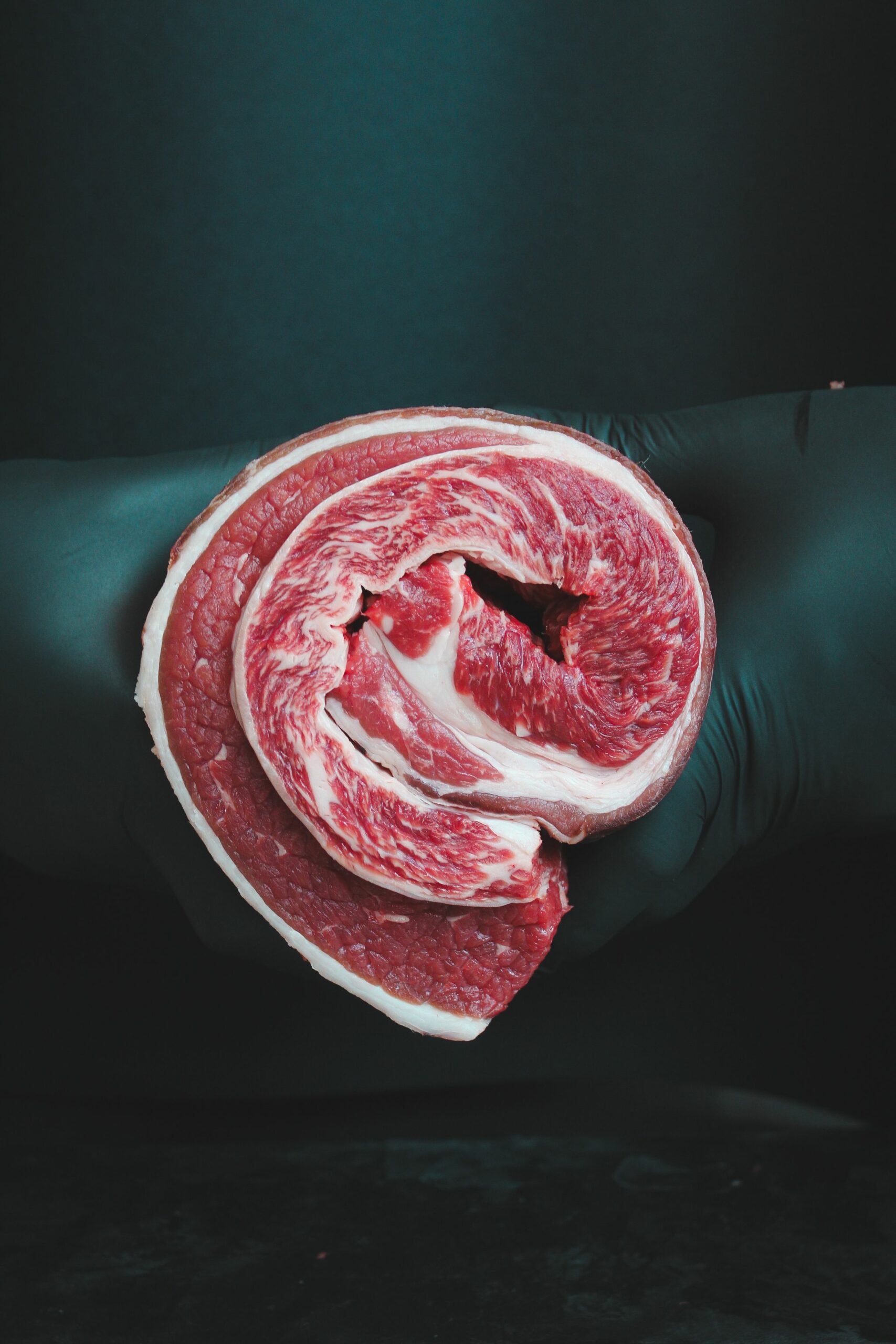 Corte fresco de vacuno crudo sostenido con guante sobre fondo oscuro
