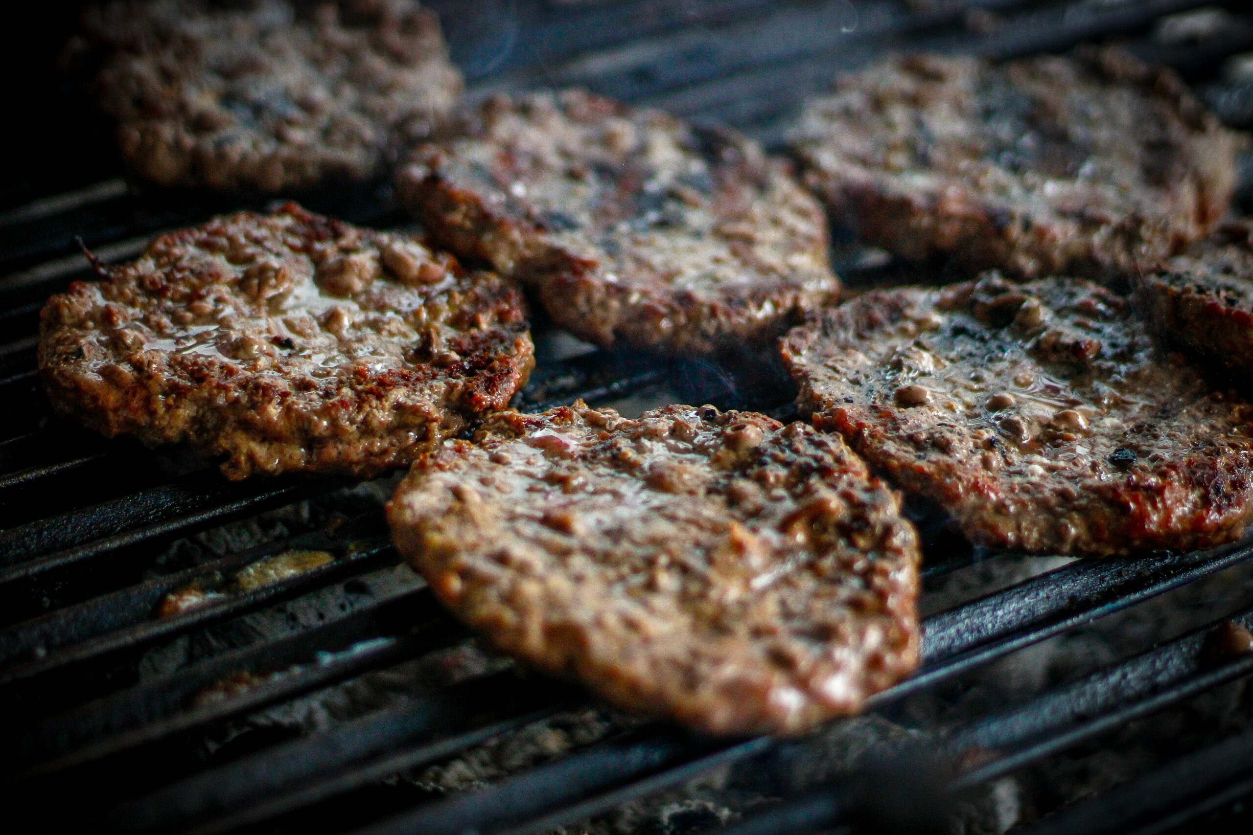 Varias hamburguesas de carne cocinándose sobre una parrilla caliente